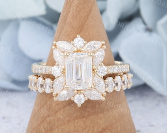 May include: A gold engagement ring set with a large emerald cut center stone surrounded by smaller round and pear shaped diamonds. The ring is set on a wooden display stand.