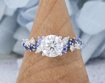 May include: A silver engagement ring with a large round center stone and a band adorned with smaller round stones and blue sapphire accents.