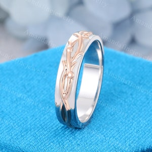 Op de afbeelding: Een zilveren trouwring met een roosgoud wijnstok ontwerp. De ring ligt op een blauwe achtergrond.