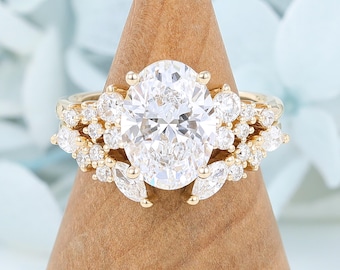 May include: A gold ring featuring a large oval-cut center stone surrounded by a cluster of smaller round and marquise-cut stones. The band is crafted from yellow gold, and the setting includes multiple prongs securing the clear, faceted stones.