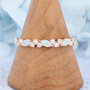 Peut inclure: Bague en or rose ornée d'opales et de diamants alternés. Le design de la bague présente des opales ovales et des diamants ronds, créant un look délicat et élégant. La bague est présentée sur un présentoir en bois.