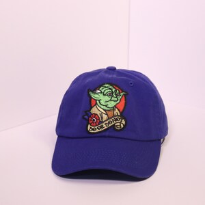 May include: A blue baseball cap with an embroidered patch of Yoda from Star Wars. The patch features Yoda with a red flower and the text "Do or Do Not".