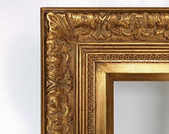 May include: A close-up of a gold-colored, ornate picture frame. The frame has detailed carvings and a textured surface. The design is classic and elegant, with a rectangular opening for a picture or artwork.