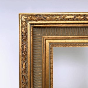 May include: A gold picture frame with a decorative, ornate design. The frame has a raised, textured border with a repeating pattern of leaves. The frame is made of wood and has a light brown finish.