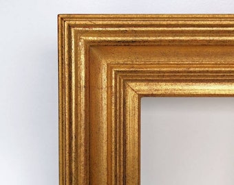 May include: Close-up of a gold-colored picture frame with a detailed, textured surface. The frame has a rectangular shape with a layered design and a bright, reflective finish. The frame is against a white background.