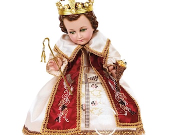 Puede incluir: Una muñeca de porcelana vestida de rey, con una corona dorada, una túnica blanca y roja, y sosteniendo un cetro dorado. La muñeca está sentada sobre un fondo blanco.