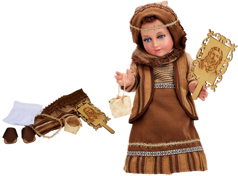 May include: A brown and beige doll dressed in a traditional outfit with a brown head scarf, holding a small basket and a wooden plaque with a carved image. The doll is part of a nativity set.