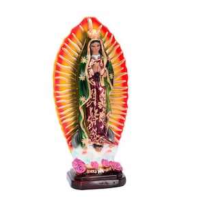 May include: A figurine of the Virgin Mary, Our Lady of Guadalupe, standing on a cloud with roses. She is wearing a blue and green robe with gold accents and a crown. The background is a red and yellow halo.