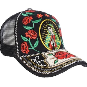May include: Black trucker hat with embroidered red roses and a religious image. The hat features a mesh back, a curved brim, and decorative stitching. The front panel displays an image of the Virgin Mary.