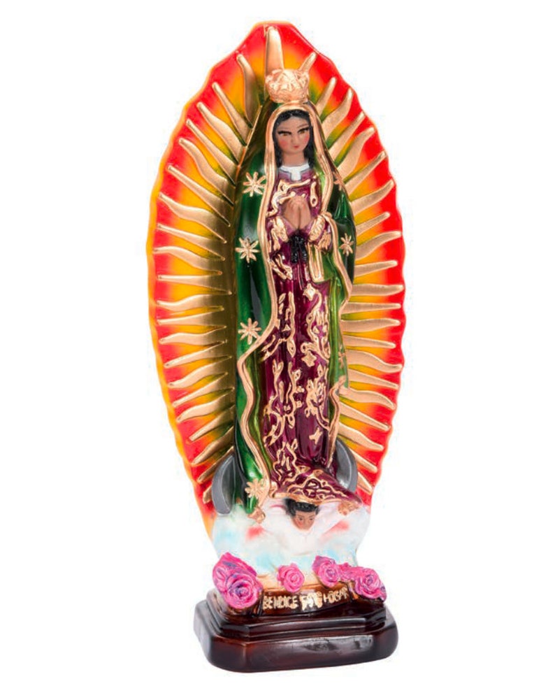 May include: A figurine of the Virgin Mary, Our Lady of Guadalupe, standing on a cloud with a crown and a blue robe over a burgundy dress. She is holding her hands in prayer. The figurine is surrounded by a golden halo with red and yellow rays. The base of the figurine is brown and has the words "REINO DE DIOS" written on it.