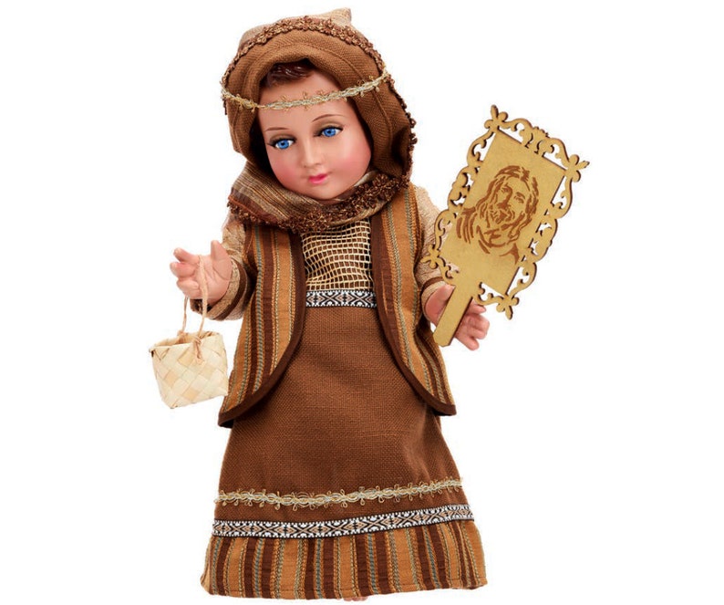 May include: A brown and tan doll dressed in a long brown robe with a woven basket and a wooden plaque with a carved image of a face. The doll has a brown head with a brown and gold head covering.