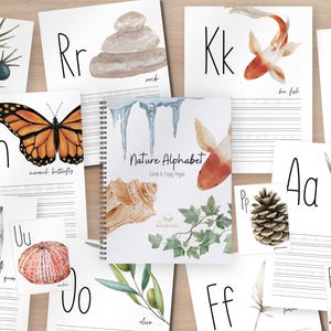 May include: A spiral-bound Nature Alphabet Cards & Copy Pages workbook surrounded by individual alphabet flashcards featuring watercolor illustrations of nature elements like a monarch butterfly, koi fish, pinecone, aloe vera, and crystals.