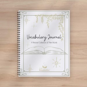 Puede incluir: Un cuaderno de espiral con portada blanca que muestra el texto Vocabulary Journal A Personal Collection of New Words. El diseño incluye dibujos lineales dorados de un libro, enredaderas colgantes y estrellas, con un pequeño logotipo.