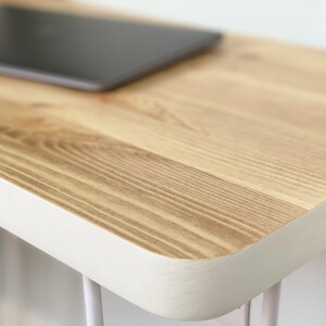 May include: A close-up of a wooden table top with a white painted edge. The table top is made of light wood with a natural grain pattern.