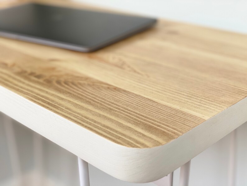 May include: A close-up of a wooden table top with a white painted edge. The table top is made of light wood with a natural grain pattern.