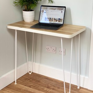May include: A white desk with a wooden top and hairpin legs. A laptop computer is on the desk. A potted plant is on the desk to the left of the laptop.