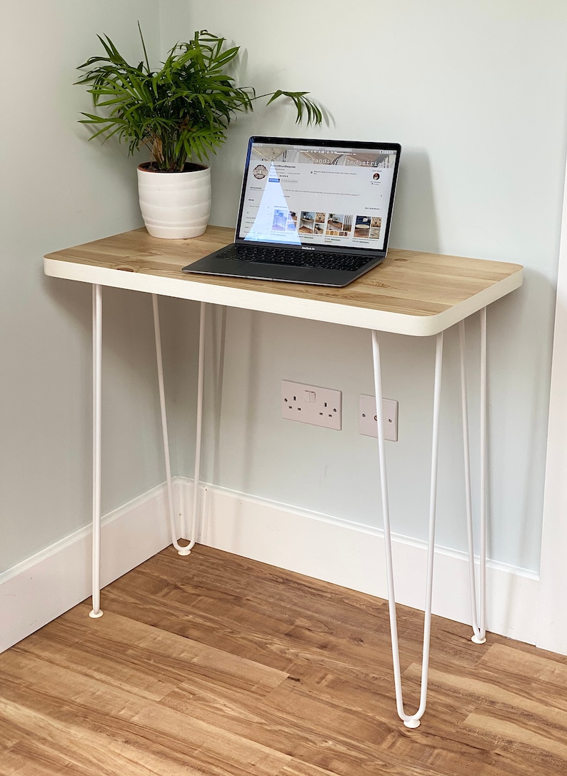 May include: A white desk with a wooden top and hairpin legs. A laptop computer is on the desk. A potted plant is on the desk to the left of the laptop.