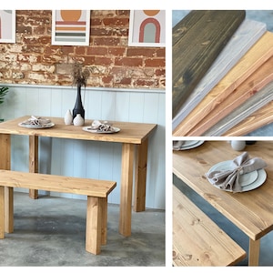 May include: A wooden table and bench set with a natural wood finish. The table has a rectangular top and four legs. The bench has a rectangular seat and four legs. The table and bench are set against a white wall with a brick accent wall behind it.