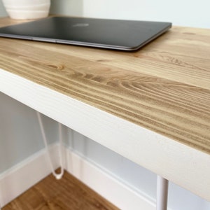 May include: A white desk with a natural wood top and hairpin legs. A laptop computer is sitting on the desk.