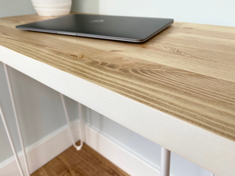 May include: A white desk with a natural wood top and hairpin legs. A laptop computer is sitting on the desk.