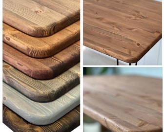 May include: Close-up of five different wood tabletops with rounded edges. The tabletops are stained in various shades of brown, gray, and black.