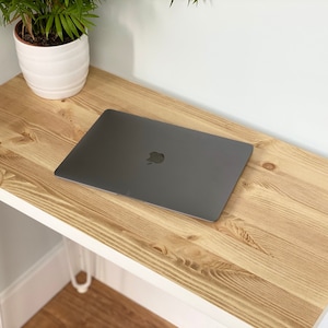 May include: A light wood desk with a white metal frame and a laptop computer on top. The desk is in a room with white walls and a potted plant.