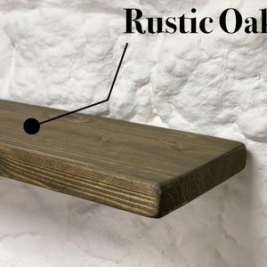 May include: A rustic oak wood shelf with a dark brown stain. The shelf is mounted on a white brick wall.