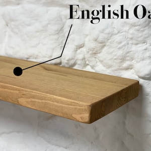 May include: A close-up of a light brown wooden shelf made of English Oak. The shelf is mounted on a white brick wall.