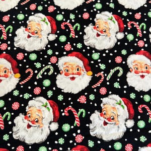 May include: Black fabric with a repeating pattern of Santa Claus faces, candy canes, and peppermint candies. The Santa Claus faces are red and white with a white beard and a red hat.