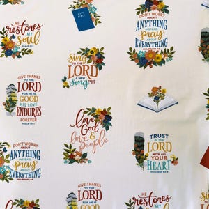 May include: White fabric with a repeating pattern of floral wreaths and bible verses. The verses include "He restores my soul", "Give thanks to the Lord", "Sing to the Lord", "Love God, love people", "Don't worry about anything, instead pray about everything", "Trust in the Lord with all your heart".