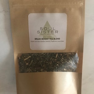 May include: A brown paper bag with a white label that says "SOUL SISTER EARTH MEDICINE BRAIN BOOST TEA BLEND Organic Gotu Kola, Eleuthero, Rosemary, Peppermint, Lemon Balm". The bag contains loose leaf tea.