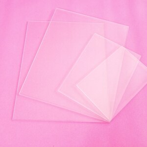 May include: Five clear acrylic sheets of varying sizes stacked on top of each other on a pink background.