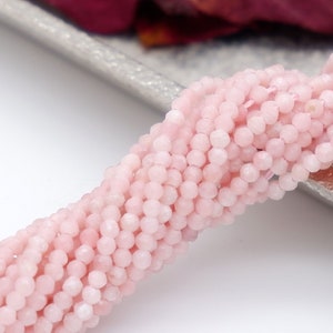 Puede incluir: Una hebra de cuentas de piedra preciosa facetadas de color rosa pálido. Las cuentas son pequeñas y redondas, y tienen un acabado liso y pulido.