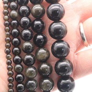 May include: Five strands of black gemstone beads with gold flecks. The beads are round and range in size from small to large.