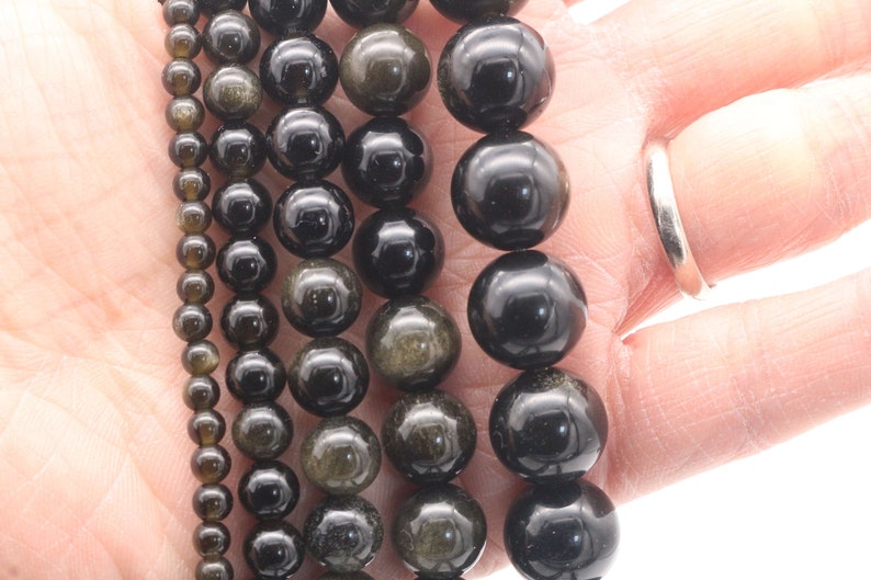 May include: Five strands of black gemstone beads with gold flecks. The beads are round and range in size from small to large.