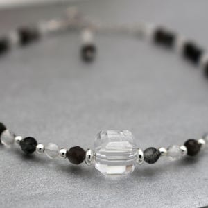 May include: A delicate bracelet with black and clear beads, featuring a large, faceted, clear crystal charm.