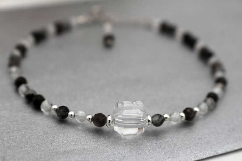 May include: A delicate bracelet with black and clear beads, featuring a large, faceted, clear crystal charm.