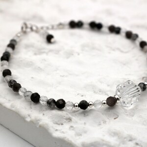 May include: A delicate bracelet made with black and clear beads, featuring a large clear crystal charm.