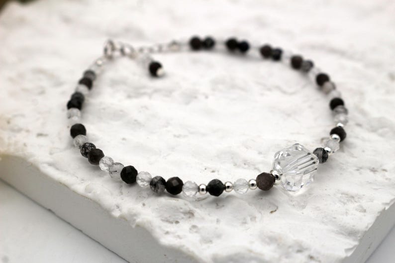 May include: A delicate bracelet made with black and clear beads, featuring a large clear crystal charm.