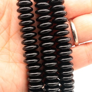 以下が含まれることがあります： 黒オニキスのビーズのネックレス。各ビーズは丸く、わずかに細長く、コイル状の効果を生み出しています。ビーズは透明な糸でつながっています。