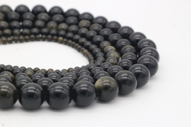 May include: A strand of black and gold gemstone beads. The beads are round and have a smooth, polished finish.