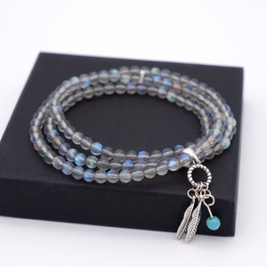Op de afbeelding: Een drievoudig armband gemaakt van grijze labradorit kralen met een zilveren bedel met twee veren en een turquoise kraal.