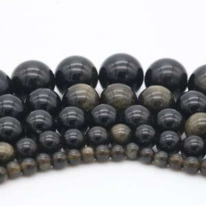 May include: A collection of black and gold gemstone beads of various sizes. The beads are round and have a smooth, polished finish.