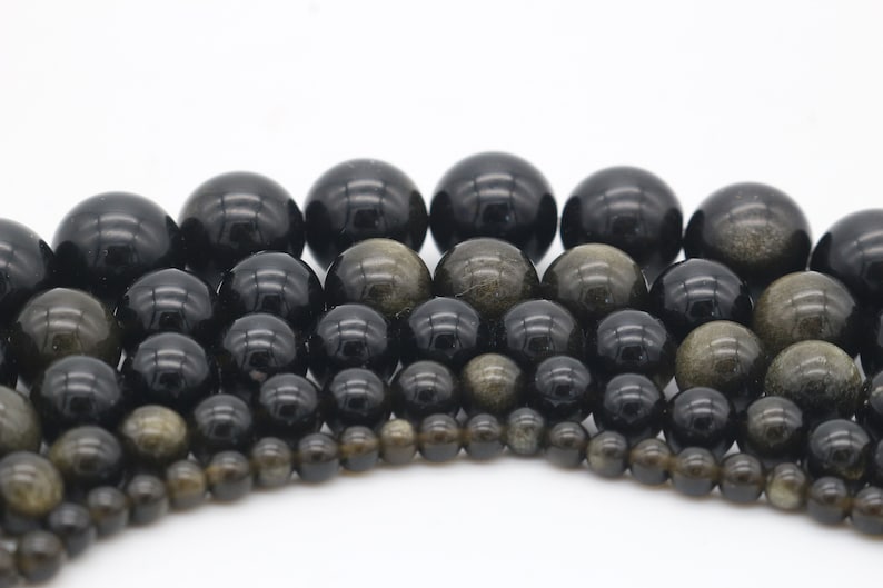May include: A collection of black and gold gemstone beads of various sizes. The beads are round and have a smooth, polished finish.