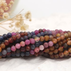 Puede incluir: Una hebra de cuentas de piedras preciosas facetadas en tonos marrones, rosas y azules. Las cuentas son redondas y tienen una forma ligeramente irregular.