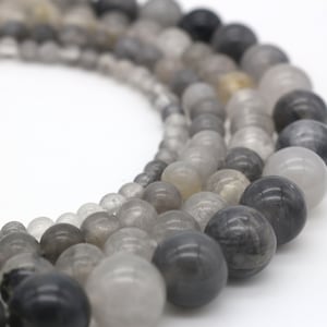 Könnte beinhalten: Eine Strähne runder, grauer und weißer Edelsteinperlen. Die Perlen sind durchscheinend und haben ein wolkiges Aussehen.