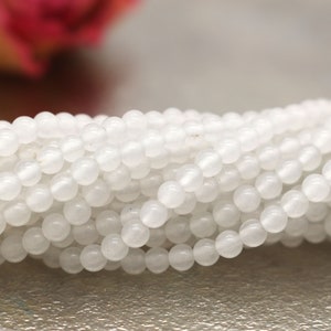 Könnte beinhalten: Eine Strähne weißer runder Perlen aus Naturstein. Die Perlen sind glatt und poliert und eignen sich perfekt für die Herstellung von Schmuck.