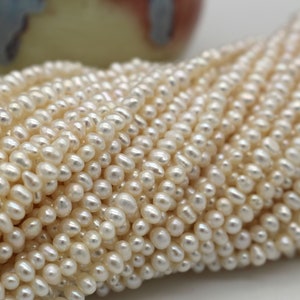 May include: A strand of white freshwater pearls, with a slightly irregular shape, arranged in a loose pile.