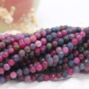 Może przedstawiać: Szereg fasetowanych koralików z kamieni szlachetnych w odcieniach różowego, fioletowego i niebieskiego. Koraliki są okrągłe i mają lekko nieregularny kształt.