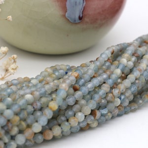 May include: A strand of light blue aquamarine beads with a faceted finish. The beads are approximately 4mm in size and have a natural, slightly irregular shape.